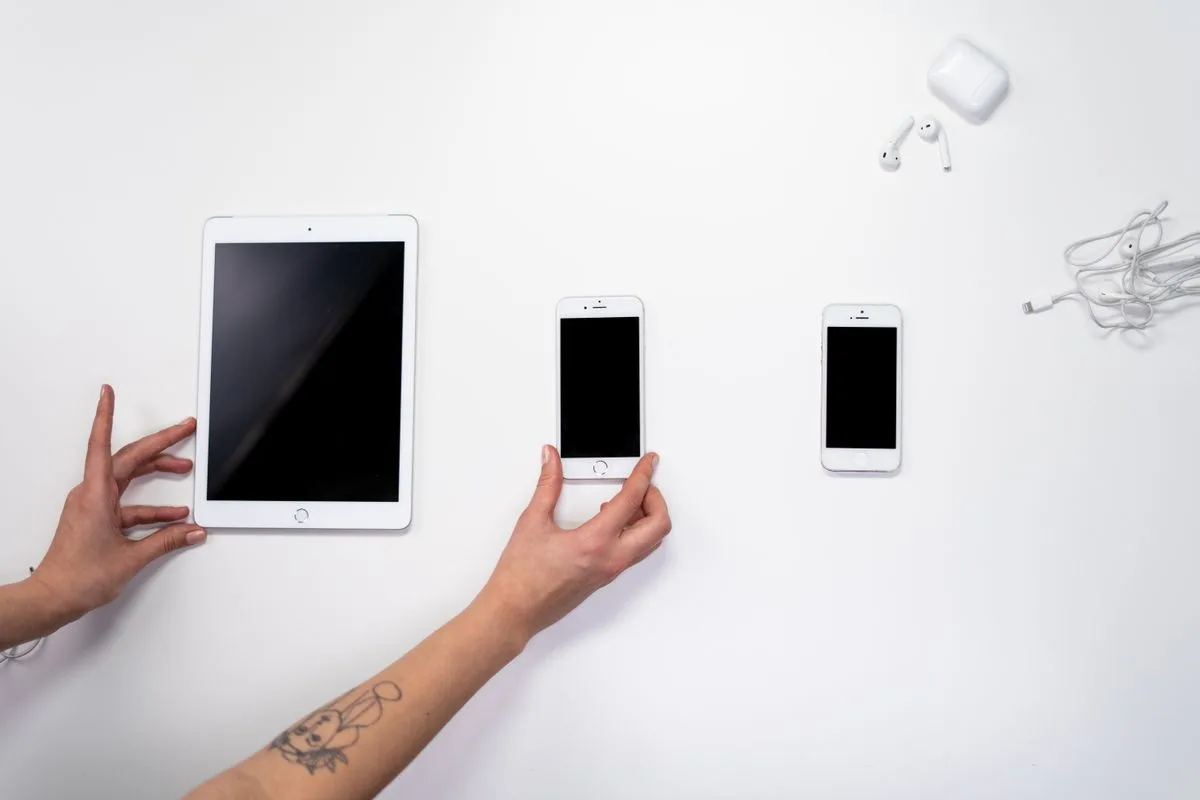 Hand ordnet ein Tablet und zwei Smartphones auf einem weißen Tisch an