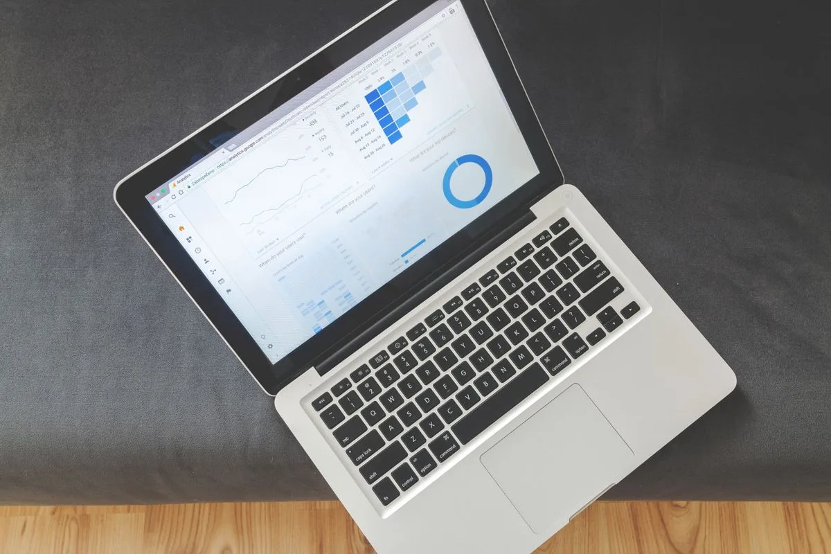 Aufgeklapptes MacBook von oben auf einer Holzplatte, auf dem Bildschirm ein Statistik-Dashboard mit Balken- und Kreisdiagramm